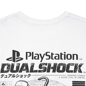 Pode incluir: Uma t-shirt branca com uma impressão gráfica preta que inclui o logótipo da PlayStation, o texto DUALSHOCK e o texto japonês デュアルショック. Abaixo, o texto VIBRATION FEEDBACK A HIGHER LEVEL OF CONTROL está impresso ao lado de uma ilustração de um globo.