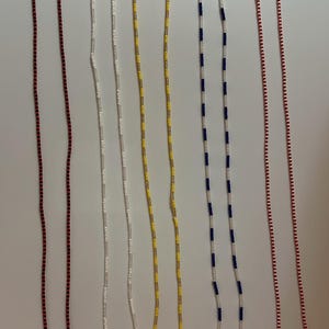 May include: A collection of six beaded necklaces in various colors. The necklaces include red and black, white, yellow, blue and white, and red and white patterns. Each necklace is made of small beads strung together.