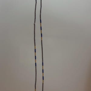 May include: A long necklace with a delicate design. The necklace features small, dark beads interspersed with sections of blue and gold beads. The necklace is displayed against a plain white background.