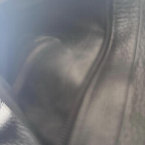 May include: A black leather wallet, open to reveal the interior. The wallet has a zipper closure and appears to be made of a soft, textured leather. The interior is also black, with a visible seam.