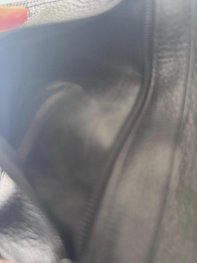 May include: A black leather wallet, open to reveal the interior. The wallet has a zipper closure and appears to be made of a soft, textured leather. The interior is also black, with a visible seam.