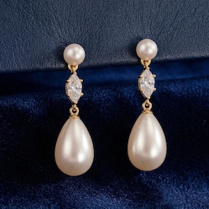 May include: A pair of elegant drop earrings. Each earring features a small, round pearl at the top, a marquise-cut clear gemstone, and a large, pear-shaped pearl pendant. The metal is gold-toned.