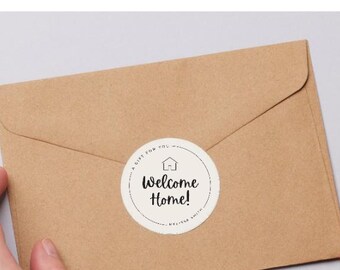 Può includere: Una busta marrone con un adesivo rotondo bianco con la scritta "Welcome Home!" in nero. Il testo "Welcome Home Sticker Gift Tag" è sopra la busta. Il testo "Easy to edit in Canva" è sotto.