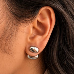 Peut inclure: Une boucle d'oreille double face de couleur argentée composée de deux éléments ovales lisses et polis. Le plus petit ovale repose sur le lobe, tandis que la pièce ovale plus grande et incurvée se place sous le lobe, créant un aspect superposé.