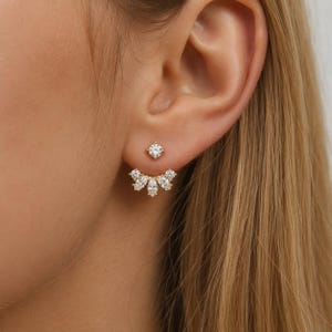 May include: A gold-toned ear jacket earring featuring a small round brilliant-cut clear stone stud at the front and a curved, fan-shaped attachment behind the earlobe, adorned with five marquise-cut and round clear stones in a symmetrical arrangement.