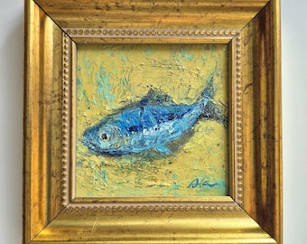 May include: A framed oil painting of a blue fish on a yellow background. The fish is painted with visible brushstrokes, and the frame is gold with a decorative edge. The artwork is signed in the lower right corner.