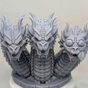 May include: A detailed, gray sculpture of a three-headed dragon. Each head features intricate details, horns, and sharp teeth. The dragon's heads are connected to a textured body, creating a mythical creature.