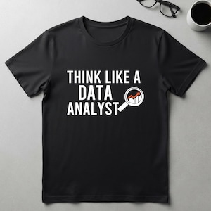 Peut inclure: Un t-shirt noir à manches courtes avec le texte blanc "THINK LIKE A DATA ANALYST" imprimé sur la poitrine. À côté du mot "ANALYST" se trouve une icône de loupe blanche contenant un petit graphique à barres avec une flèche orange ascendante.