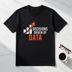 Puede incluir: Una camiseta negra de manga corta con un gráfico de barras blanco y una flecha naranja hacia arriba. El texto DECISIONS DRIVEN BY aparece en blanco, con la palabra DATA en letras grandes de color naranja debajo.