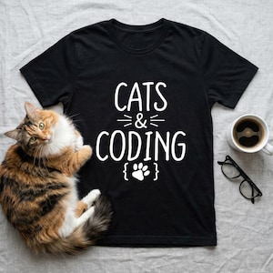 May include: Black t-shirt with the words "CATS & CODING" in white, with a paw print graphic. A calico cat is lying next to the shirt. A cup of coffee and glasses are also in the image.