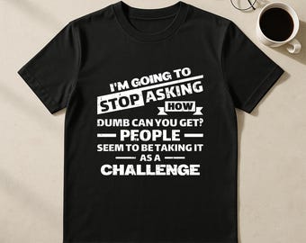 May include: A black short-sleeved t-shirt featuring white distressed text that reads: I'M GOING TO STOP ASKING HOW DUMB CAN YOU GET? PEOPLE SEEM TO BE TAKING IT AS A CHALLENGE. The shirt has a crew neckline and a standard fit with a graphic print on the front.