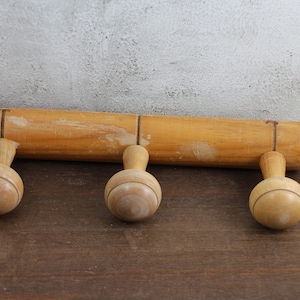 Puede incluir: Un perchero de madera con tres pomos redondos. El perchero est&aacute; hecho de madera natural y tiene un aspecto r&uacute;stico.