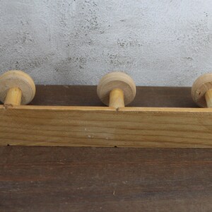 Puede incluir: Perchero de pared de madera con tres pomos redondos. El perchero est&aacute; hecho de madera natural y tiene un aspecto r&uacute;stico.