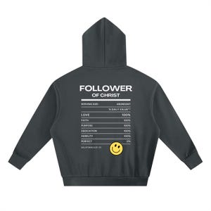 May include: Dark gray hoodie with the text "FOLLOWER OF CHRIST" and a nutrition facts-style graphic. The graphic lists values for love, faith, purpose, dedication, humility, and perfect. A yellow smiley face is at the bottom. The text "GALATIANS 5:22-23" is also present.