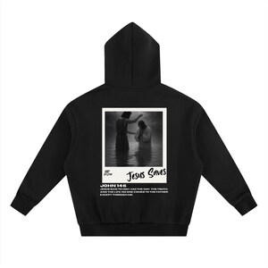 May include: Black hoodie featuring a graphic of a baptism scene with the text "Jesus Saves." The hoodie also includes the text "JOHN 14:6" and a quote from the Bible. The hoodie has a hood and long sleeves.