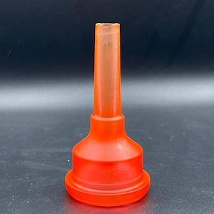 May include: A translucent orange plastic funnel with a wide base and a long, narrow spout. The funnel is designed with a flared base and a cylindrical neck, suitable for pouring liquids. The object is set against a dark background.