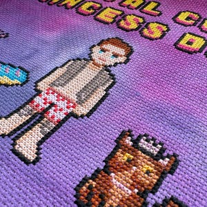 May include: Cross-stitch artwork featuring a pixelated figure in red and white swim trunks and a pixelated dog. The background is a gradient of purple and pink. The text "REAL COOL PRINCESS DOG" is stitched in yellow and orange.