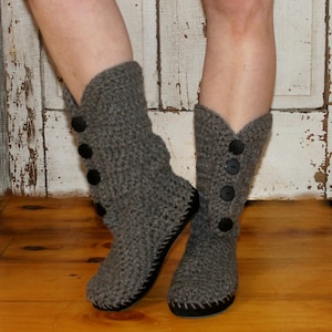 Puede incluir: Botas de crochet grises con botones negros. Las botas son holgadas y tienen una suela plana.
