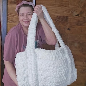 May include: A white crocheted tote bag with thick, fluffy yarn. The bag has two long straps and a large, rectangular body.