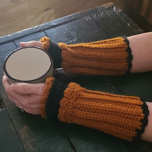 May include: Handmade crochet arm warmers in a warm orange color with black trim. The ribbed design provides texture and warmth. These cozy wrist warmers are perfect for cool weather and add a touch of handmade charm to any outfit.