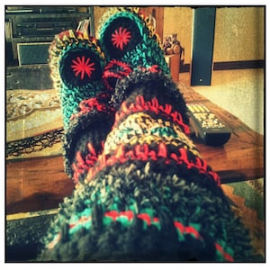 May include: Close-up of a pair of colorful crocheted slippers with a black, red, green, and white pattern. The slippers are worn and have a fuzzy texture.