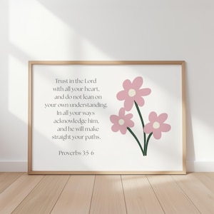 Op de afbeelding: Een ingelijste print met een licht houten frame. De print bevat de tekst "Trust in the Lord" en een bloemenillustratie van drie roze bloemen met groene stelen. Het citaat komt uit Spreuken 3:5-6.