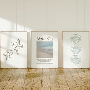 Op de afbeelding: Drie ingelijste kunstafdrukken met een kustthema. De linkerprint toont twee omtrekken van zeesterren. De middelste print heeft een strandscène en de tekst "PSALM 93:4". De rechterprint toont drie schelpenomtrekken.