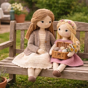 Puede incluir: Dos muñecas de ganchillo hechas a mano sentadas en un banco de madera al aire libre. Una muñeca viste un vestido color crema y una rebeca marrón. La otra muñeca viste un vestido rosa y sostiene una cesta con lana y flores. Las muñecas tienen pelo de lana y están en un jardín.