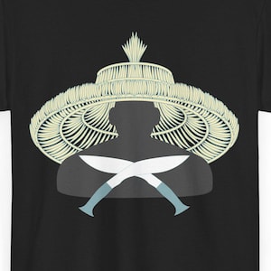 Puede incluir: Camiseta negra con un diseño gráfico de una silueta que lleva un sombrero tejido y cuchillos cruzados. El sombrero es de color beige claro y los cuchillos tienen mangos azul claro. El diseño está centrado.