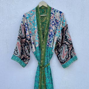 May include: A long-sleeved robe featuring a vibrant patchwork design with various paisley and floral patterns in shades of green, blue, black, and white. The garment includes a matching fabric tie belt at the waist and a solid green trim.