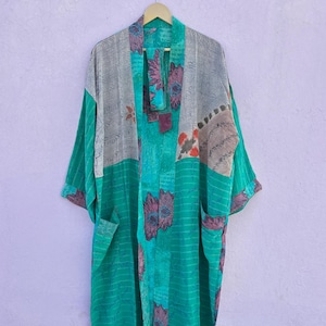 May include: A long, open-front kimono robe in shades of teal, gray, and floral patterns. The robe has long sleeves and pockets. The fabric appears to be a lightweight material, suitable for layering. The robe is hanging on a wooden hanger.