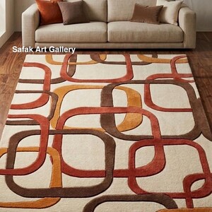 May include: A rectangular area rug featuring a cream-coloured background with an overlapping geometric pattern of rounded squares in shades of burnt orange, terracotta, and dark brown. The text Safak Art Gallery is visible on the left side.