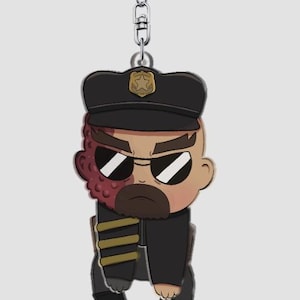 Pode incluir: Um porta-chaves de novidade com um personagem em estilo cartoon em uniforme de pol&iacute;cia. O personagem tem uma express&atilde;o severa, &oacute;culos de sol e uma cicatriz no rosto. O porta-chaves tem um fecho prateado.