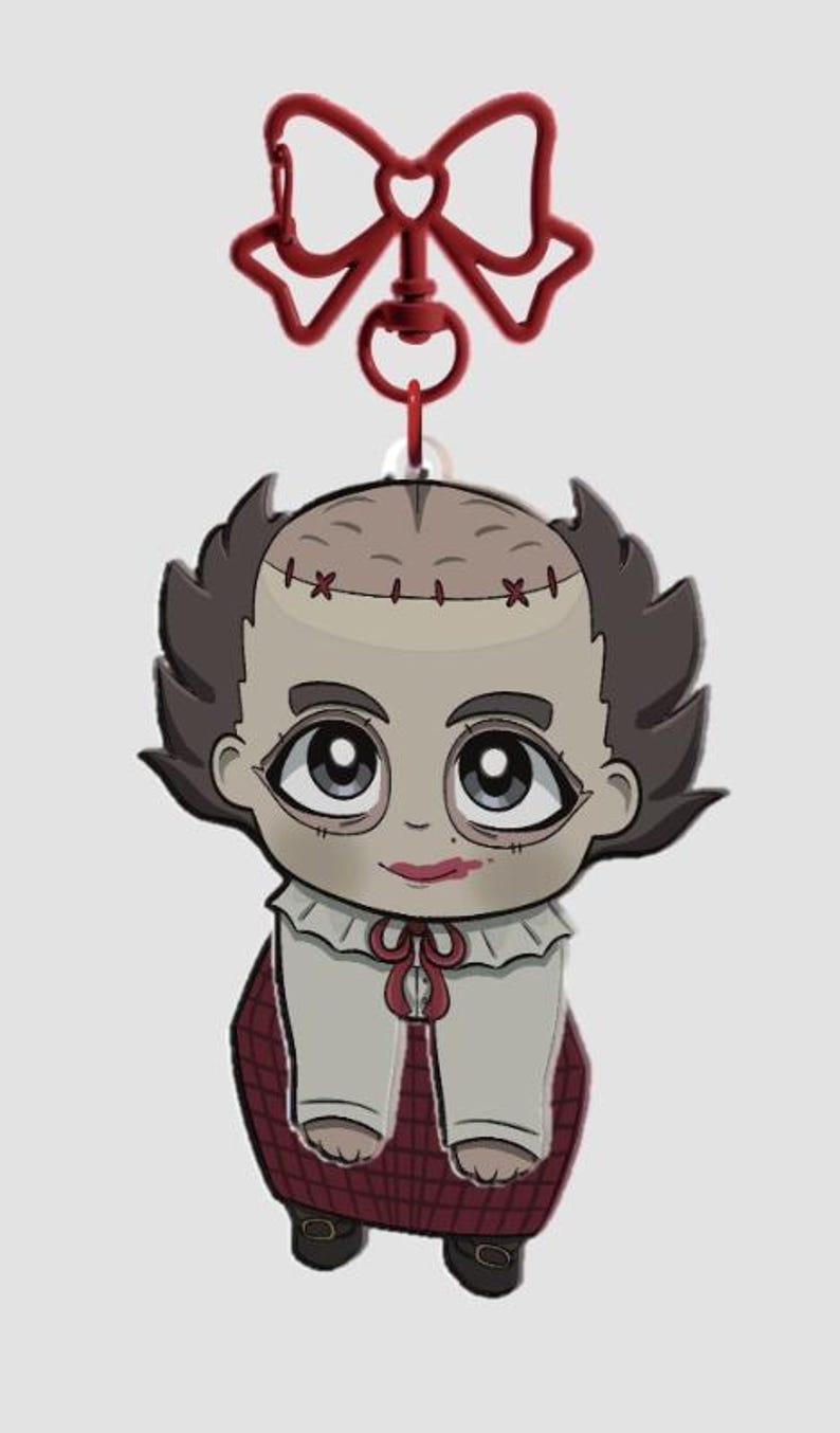 Pode incluir: Um chaveiro em estilo cartoon com um personagem com cabe&ccedil;a costurada, cabelo escuro e um la&ccedil;o vermelho. O personagem usa uma camisa branca com um la&ccedil;o vermelho e uma saia xadrez. O chaveiro tem um fecho em forma de la&ccedil;o vermelho.