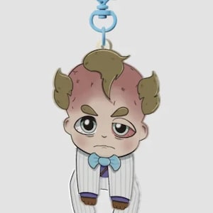 Pode incluir: Um chaveiro de desenho animado com um personagem semelhante a um beb&ecirc; em um terno com uma gravata borboleta azul. O personagem tem uma tez vermelha, cabelo castanho e uma express&atilde;o cansada. O chaveiro tem um fecho azul em forma de cora&ccedil;&atilde;o.