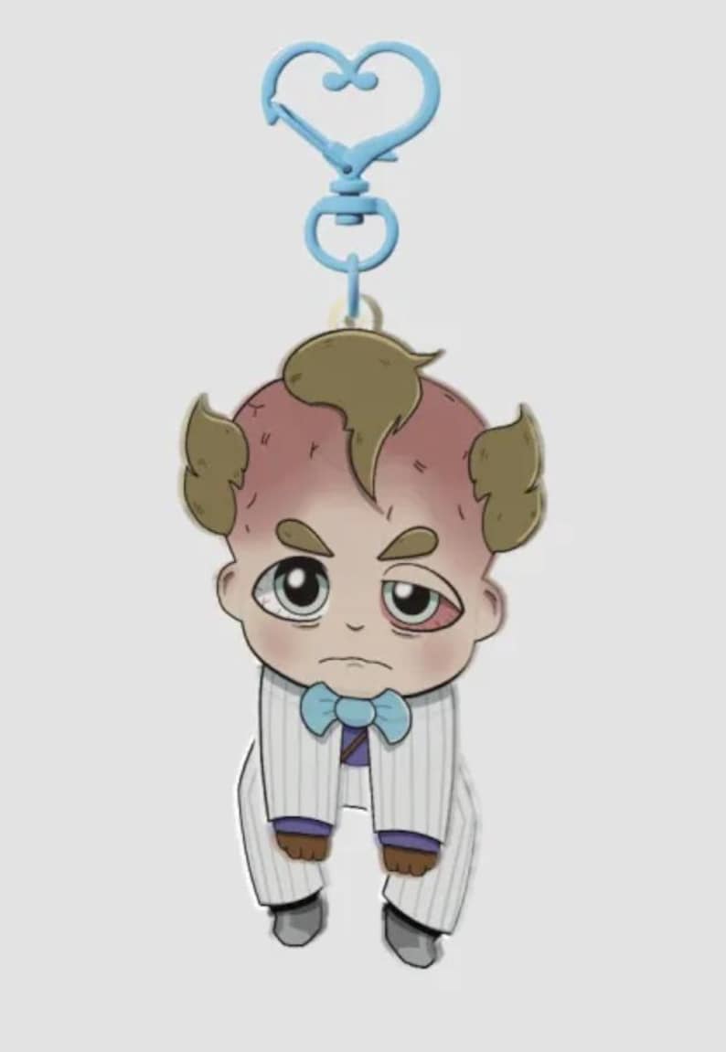 Pode incluir: Um chaveiro de desenho animado com um personagem semelhante a um beb&ecirc; em um terno com uma gravata borboleta azul. O personagem tem uma tez vermelha, cabelo castanho e uma express&atilde;o cansada. O chaveiro tem um fecho azul em forma de cora&ccedil;&atilde;o.