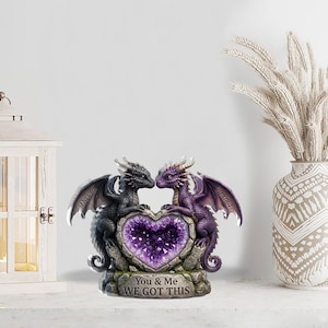 May include: A decorative figurine featuring two dragons facing each other, flanking a heart-shaped amethyst. The dragons are black and purple, with the names "David" and "Emma" on their wings. The base reads "You & Me WE GOT THIS."