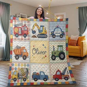 Puede incluir: Una colorida colcha de retazos con ilustraciones de vehículos: camión de bomberos, excavadora, coche de policía, camión volquete, tractor, hormigonera, camioneta y grúa. La colcha tiene un panel central con el nombre "Oliver".