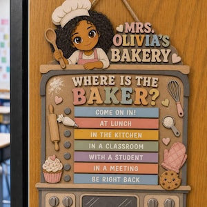 May include: A wooden wall sign titled MRS. OLIVIA'S BAKER and WHERE IS THE BAKER? featuring a cartoon baker character, a rolling pin, a cupcake, a whisk, and a cookie. The sign includes movable status bars for Come On In, At Lunch, In The Kitchen, In A Classroom, With A Student, In A Meeting, and Be Right Back.