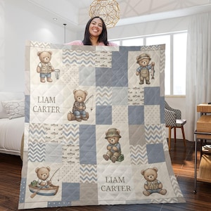 Könnte beinhalten: Eine Steppdecke mit Patchwork-Design in Blau-, Grau- und Cremetönen. Das Muster zeigt Illustrationen von Teddybären als Angler, Fischmotive und Zickzackstreifen. Der Text Liam Carter ist auf der Decke aufgedruckt.
