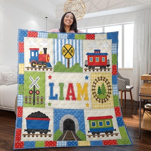 May include: A rectangular quilt featuring a train theme with colorful blocks displaying a steam engine, a railroad crossing sign, a passenger car, a coal car, a tunnel, and a circular track. The center block displays the name LIAM in large letters.