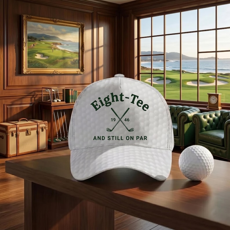 K&ouml;nnte beinhalten: Wei&szlig;e Golfkappe mit dem Text "Eight-Tee" und gekreuzten Golfschl&auml;gern. Die Kappe hat eine strukturierte Oberfl&auml;che, &auml;hnlich einem Golfball. Ein Golfball liegt auf einer Holzoberfl&auml;che. Der Hintergrund zeigt ein Golfplatzgem&auml;lde und einen Golfplatzblick.