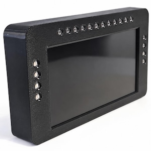 May include: A rectangular black electronic display device featuring a dark screen framed by a thick, textured casing. The frame is embedded with a series of small, circular LED lights arranged along the top edge and the right side of the unit.