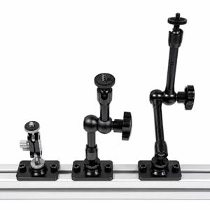 May include: Three black articulating arms with ball joints and mounting plates are displayed. Each arm has a different configuration, with adjustable knobs and screw-on heads for attaching equipment. The arms are mounted on a silver metal rail.