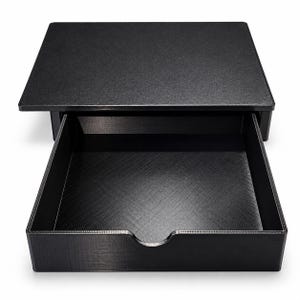 May include: A black desktop storage unit featuring a flat top surface and a single pull-out drawer. The drawer has a semi-circular cutout on the front edge for easy access, and the entire structure is made of a matte black material with a textured finish.