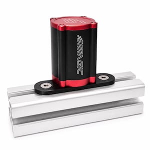 May include: A black and red cylindrical Simagic component with a logo on top and side, mounted on a black plate with two silver bolts, attached to a horizontal silver aluminum extrusion profile with a central groove and rectangular cross-section.