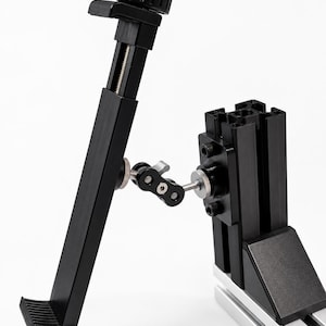 May include: A black adjustable tablet holder with a screw-on clamp and a pivoting arm. The holder is attached to a silver and black metal base, designed for stability and versatile positioning.