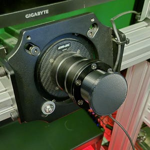 Peut inclure: Gros plan sur un composant de volant de course noir et argenté. L'appareil est doté d'un gros bouton noir rond et est monté sur un cadre argenté. La marque "SIMAGIC" est visible au centre du volant.