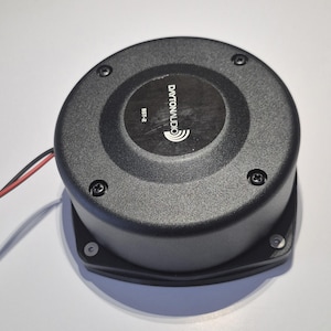 Pode incluir: Um alto-falante preto Dayton Audio BST-2 com um design circular. O alto-falante tem uma superfície texturizada e é fixado com quatro parafusos. O logotipo Dayton Audio e o número do modelo são impressos na parte superior. Fios vermelhos e pretos se estendem da lateral.