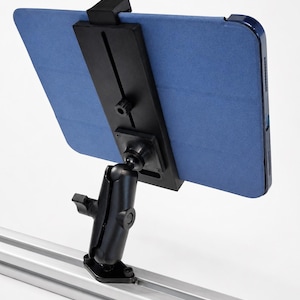 May include: A black adjustable tablet mount attached to a silver aluminum extrusion rail. The mount features a ball-and-socket joint for positioning and a black plastic clamp holding a blue tablet case in a horizontal orientation.